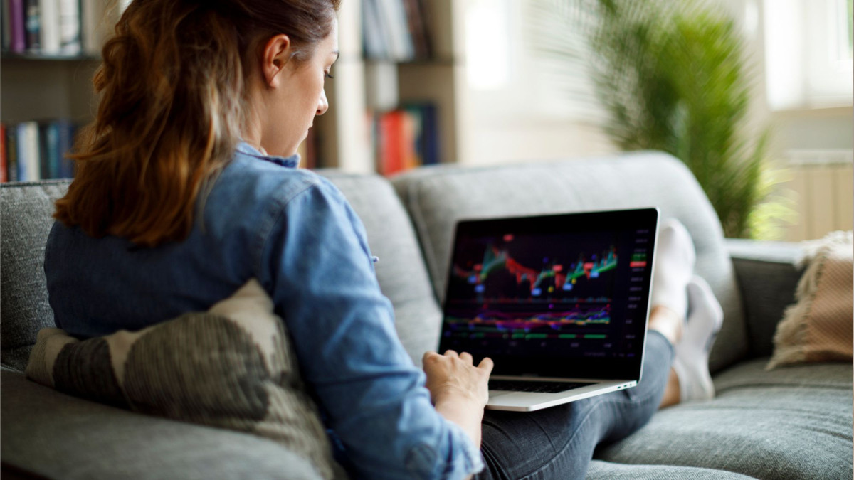 Junge Frau sitzt auf dem Sofa und schaut auf dem Laptop Aktienkurse an.