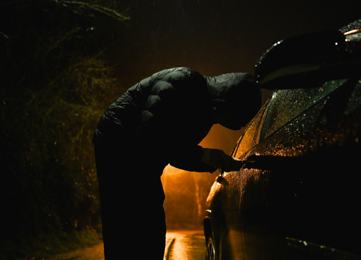 Ein maskierter Mann macht sich an einem Auto zu schaffen