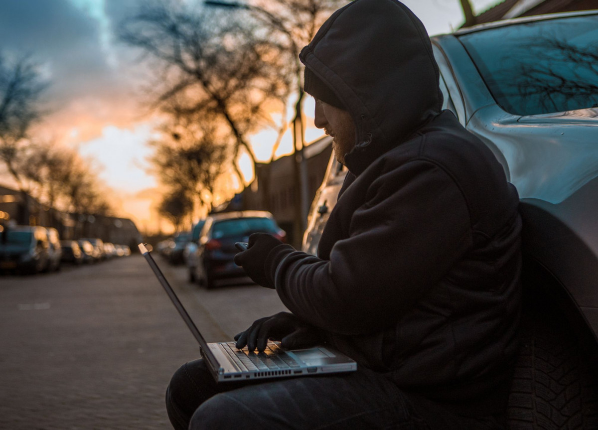 Ein Autodieb mit Laptop sitzt vor einem Auto