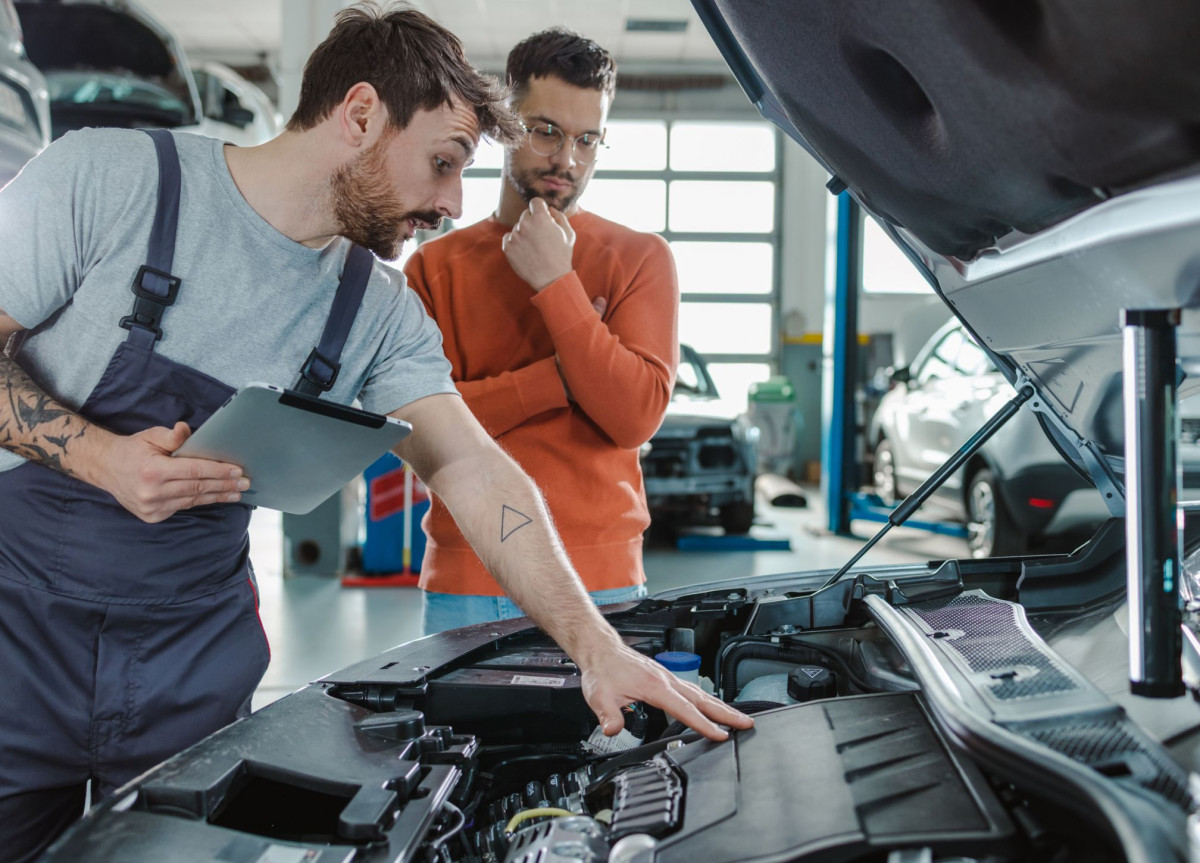 Ein Kfz-Mechaniker zeigt einem Autobesitzer etwas im Motorraum von dessen Auto.