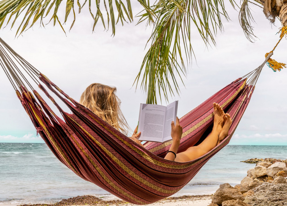 Eine Frau liest in einer Hängematte am Strand ein Buch