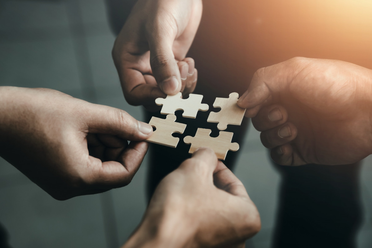 Vier Hände halten Puzzle Teile zusammen