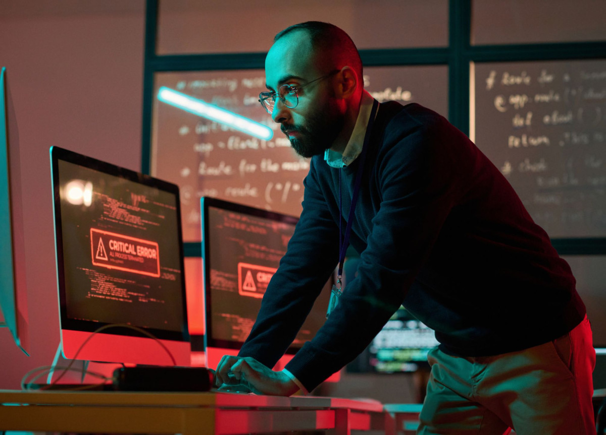 Ein Mann kontrolliert mehrere Computer, auf denen kritische Fehlermeldungen angezeigt werden.