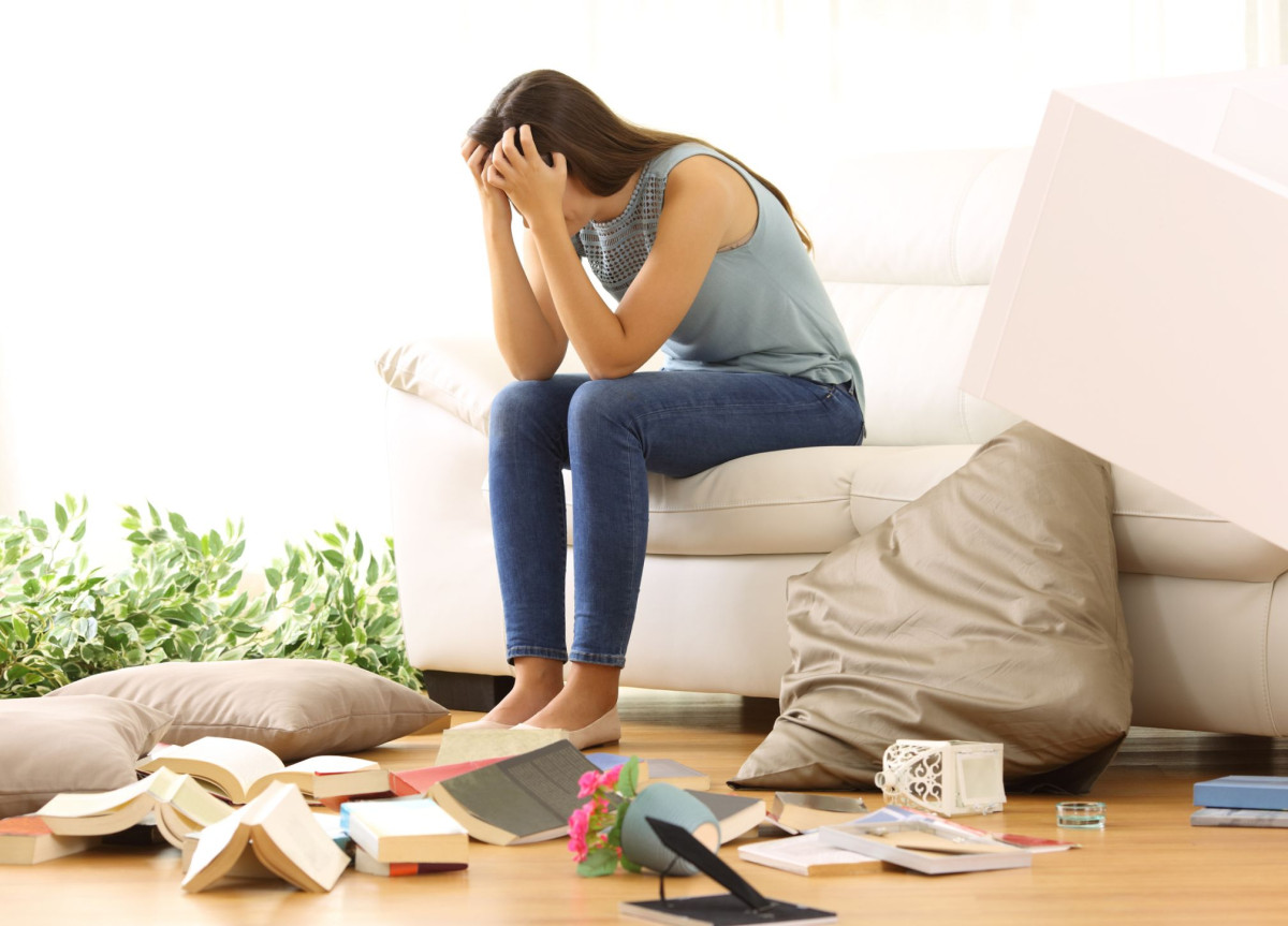 Eine Frau sitzt verzweifelt nach einem Einbruch in ihrer verwüsteten Wohnung