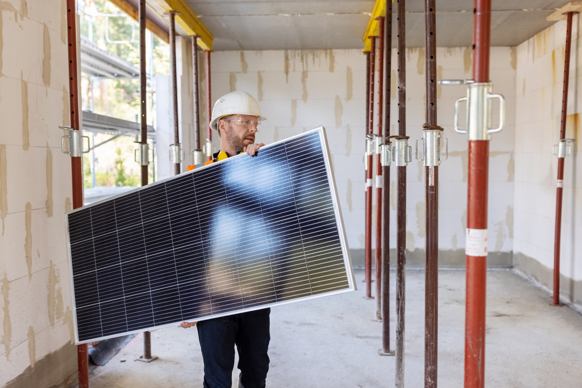 Solarpanel wird von Bauarbeiter durch Rohbau getragen