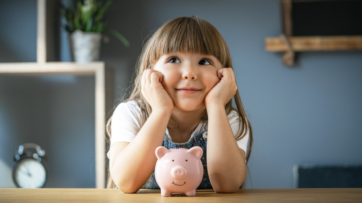 Kleines Mädchen sitzt vor einem Sparschwein