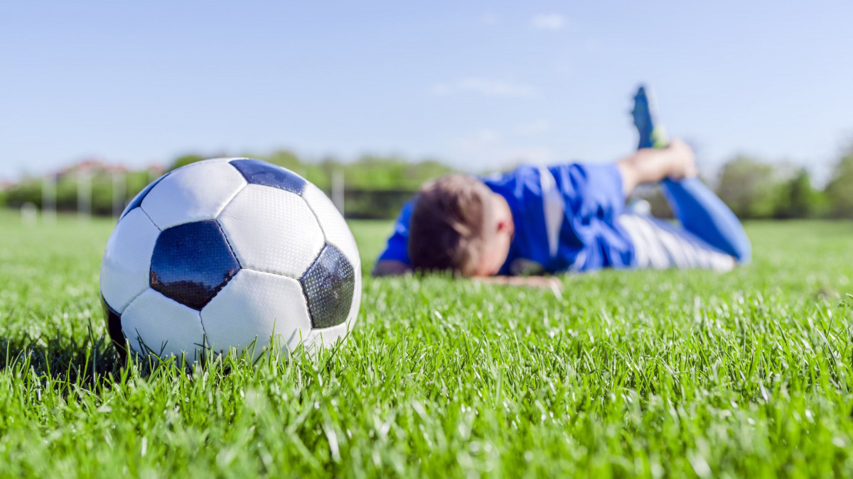 Ein verletzter Fußballer liegt auf dem Platz, vor ihm ein Fußball