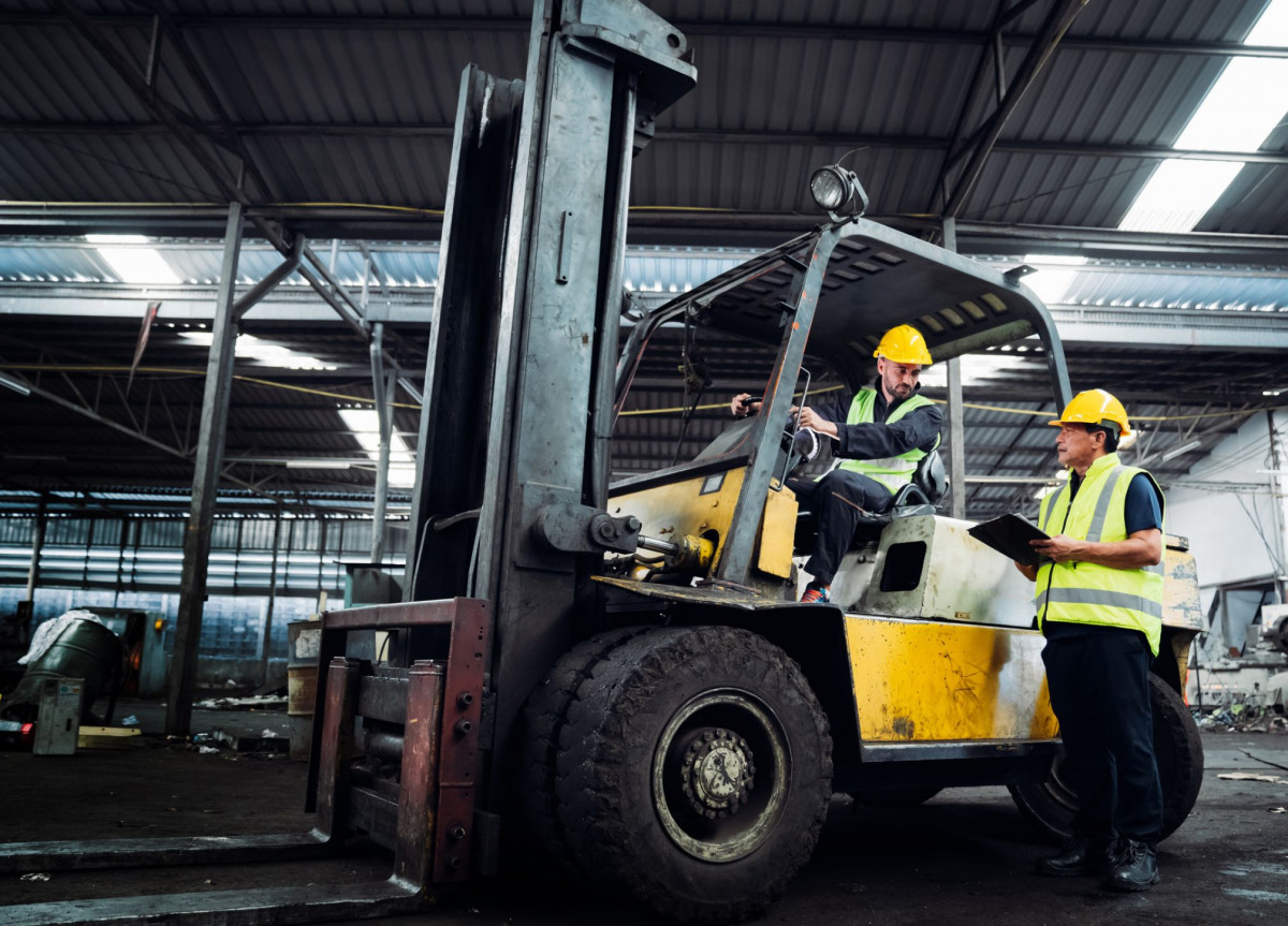 Gapelstablerfahrer diskutiert mit einem anderen Arbeiter in einer Fabrikhalle