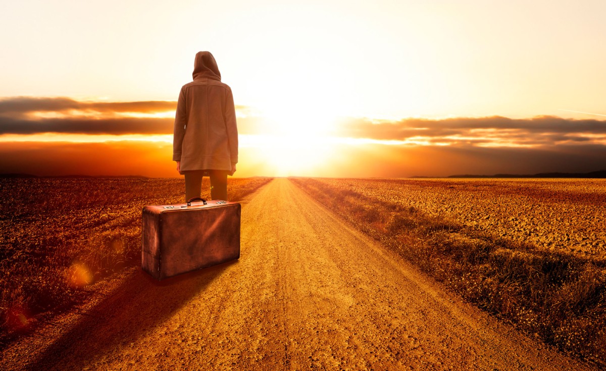 Frau mit Koffer vor Sonnenuntergang in karger Landschaft