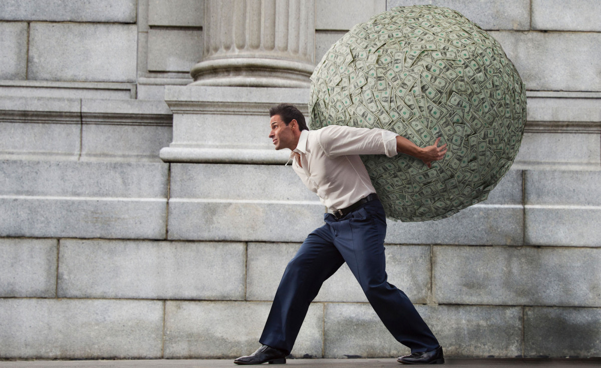 Mann trägt Riesenkugel mit Geldscheinen auf dem Rücken