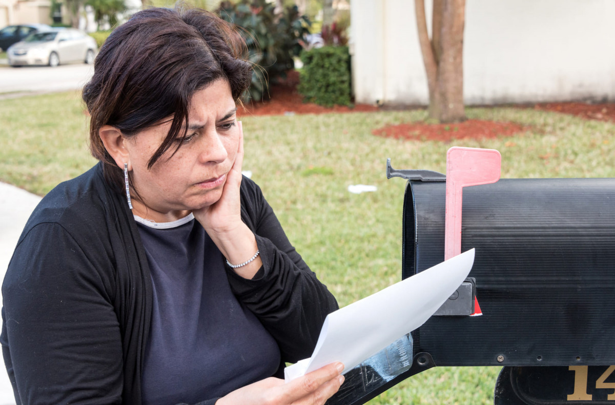 Eine Frau liest am Briefkasten einen Brief mit einer offensichtlich schlechten Nachricht