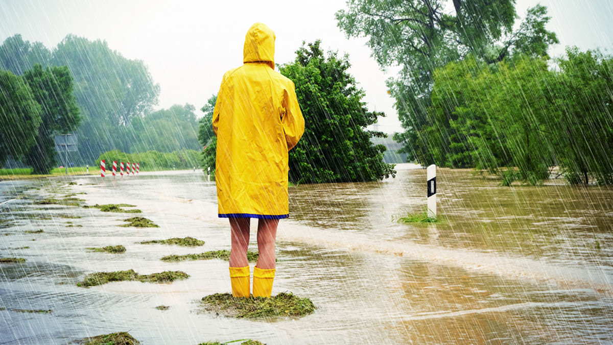 Frau in Regenkleidung auf überfluteter Straße