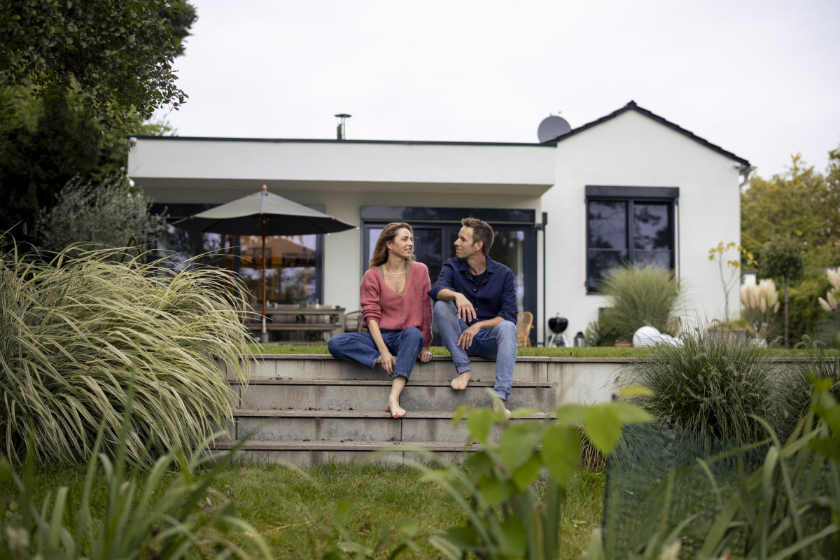 Junges Paar sitzt vor einem Einfamilienhaus