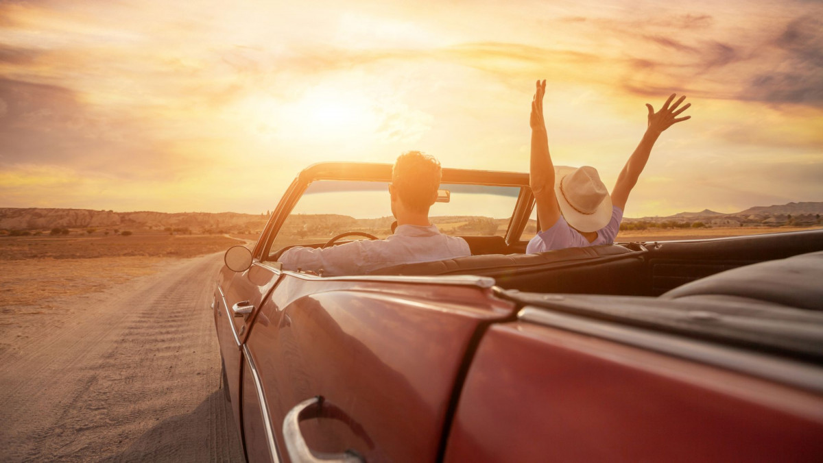 Zwei Menschen fahren in ihrem Cabrio in den Sonnenuntergang