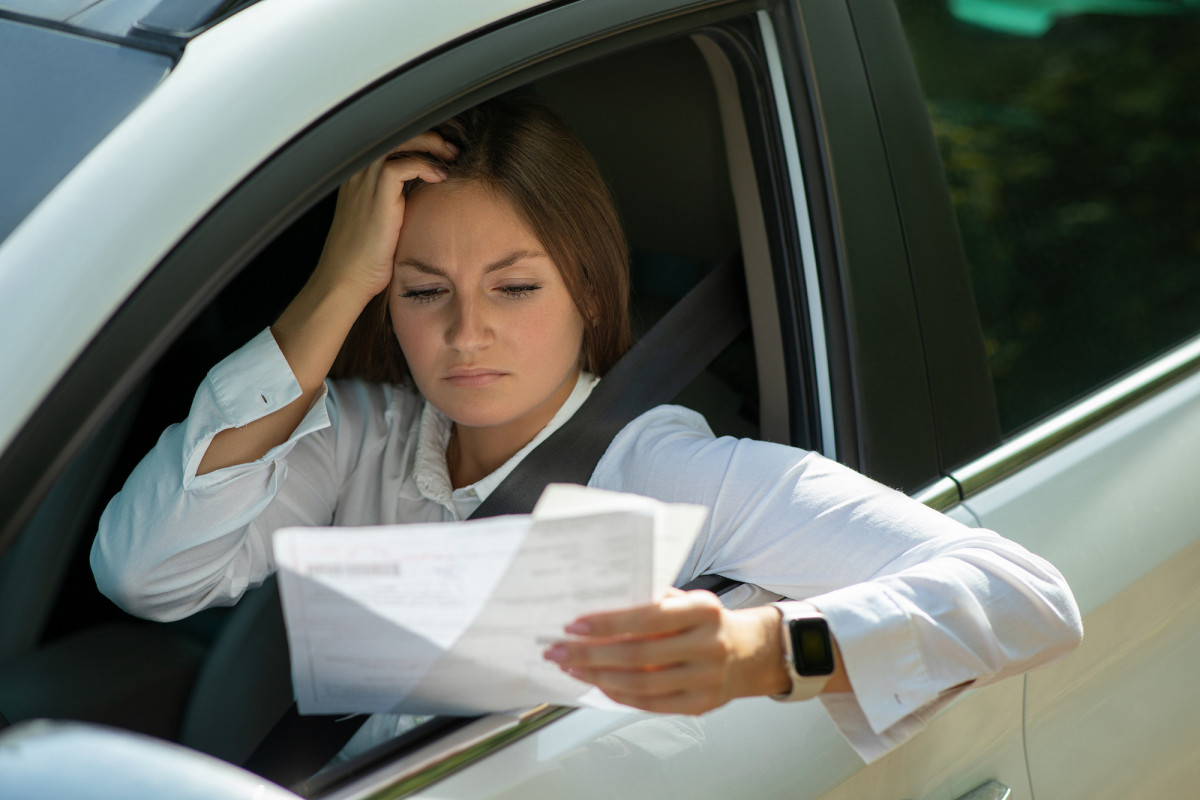 Eine Frau sitzt im Auto und guckt traurig auf einen Brief