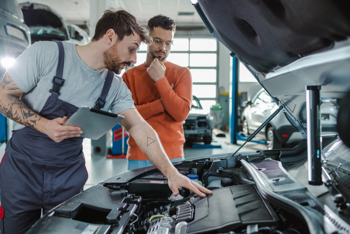 Kunde und Kfz-Techniker sprechen in einer Werkstatt über das Autoproblem