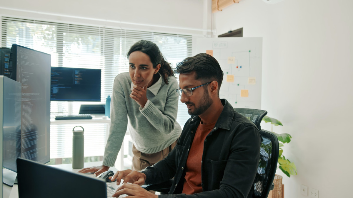 Mann und Frau blicken im Büro auf einen Bildschirm.
