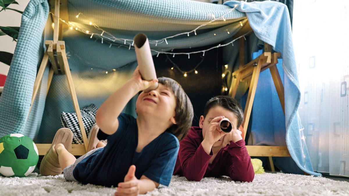 Zwei Kinder spielen in einem selbstgebauten Zelt im Wohnzimmer.