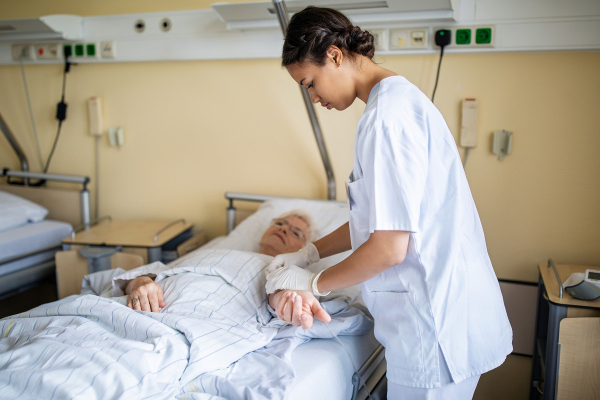 Krankenschwester betreut eine Patientin, die im Bett liegt.