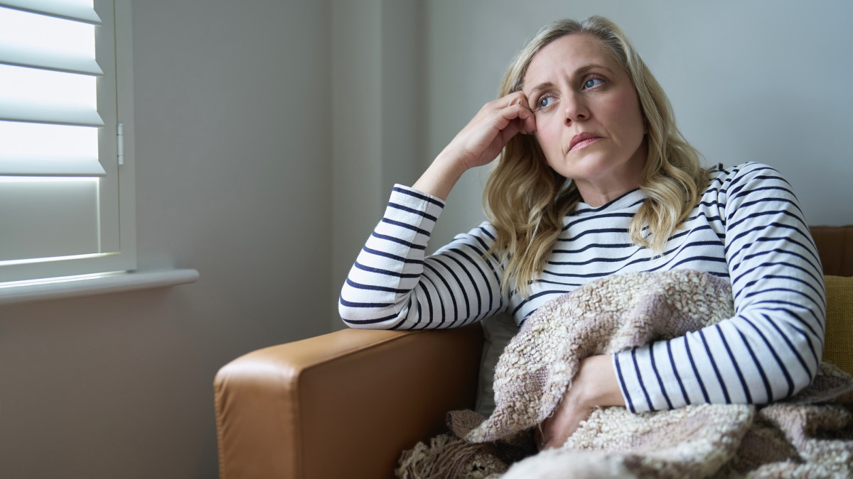 Frau, die an Langzeitkrankheit leidet, sitzt zu Hause auf dem Sofa