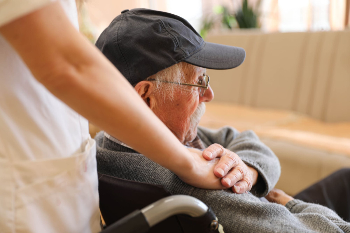 Älterer Mann im Rollstuhl spricht mit einer Krankenschwester in einem Pflegeheim