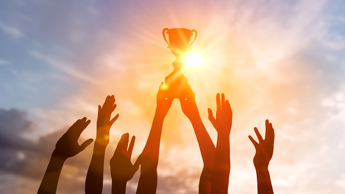 Mehrere Hände strecken sich Richtung eines Pokals, der von zwei Händen in den Himmel gehalten wird