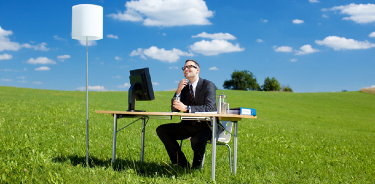 Mann sitzt an Bürotisch auf einer Wiese