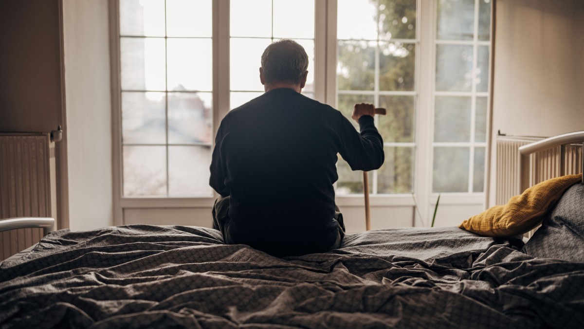 alter Mann sitzt auf dem Bett