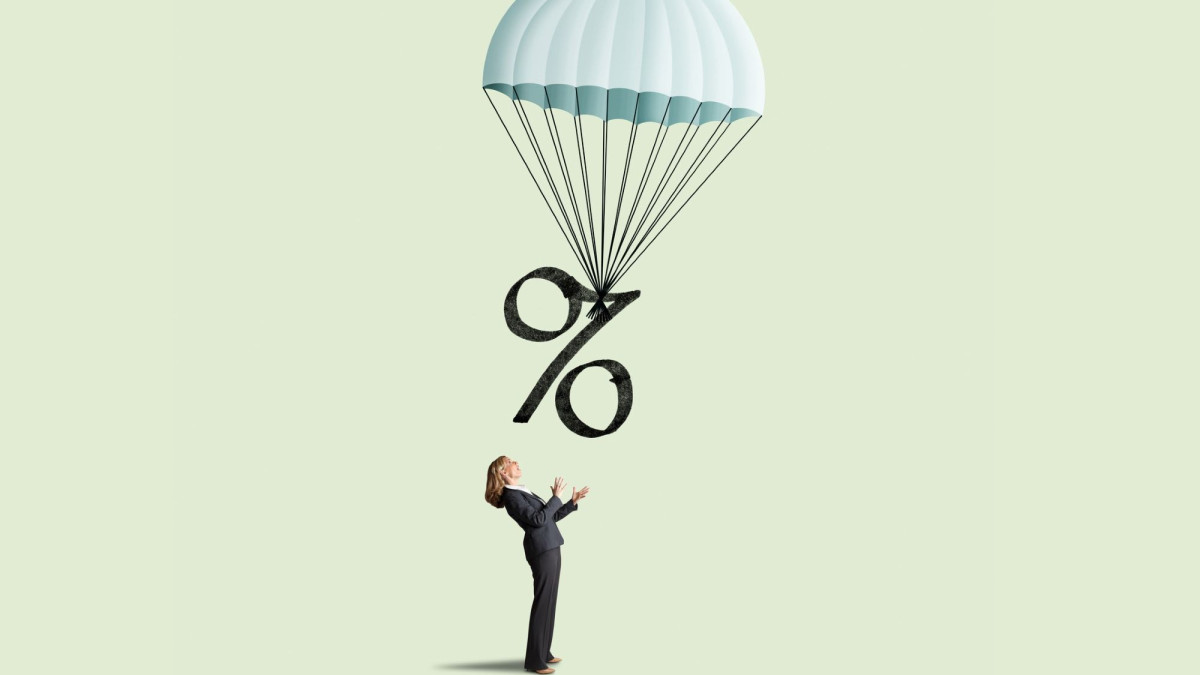 Ein Heißluftballon an dem ein Prozentzeichen hängt fliegt über einer Frau in Hosenanzug