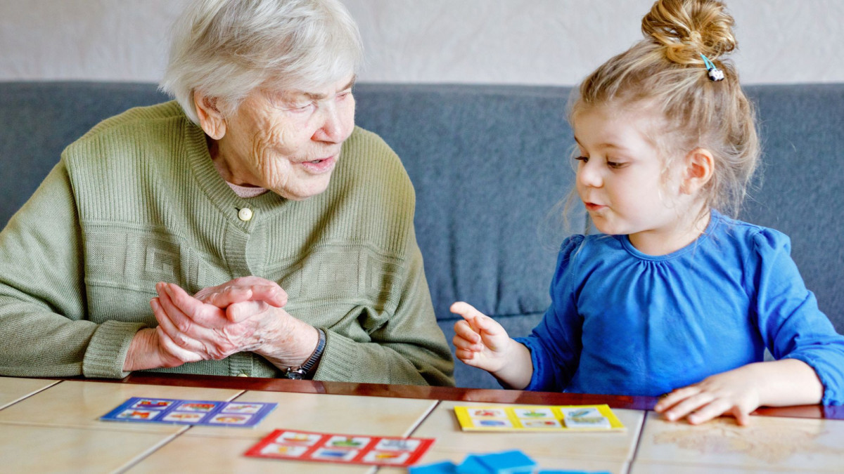 Oma spielt mit ca 3-jährige Mädchen ein Spiel am Wohnzimmertisch