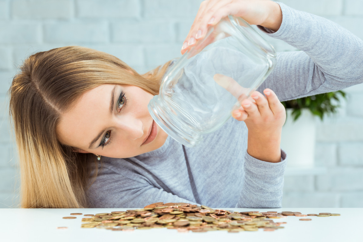 Eine Frau schüttet ein Spar-Glas mit Kleingeld aus und guckt in das leere Glas