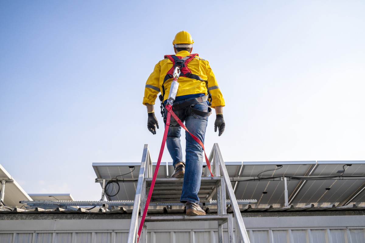 Ein Mann klettert eine hohe Leiter mit einer Sicherung.