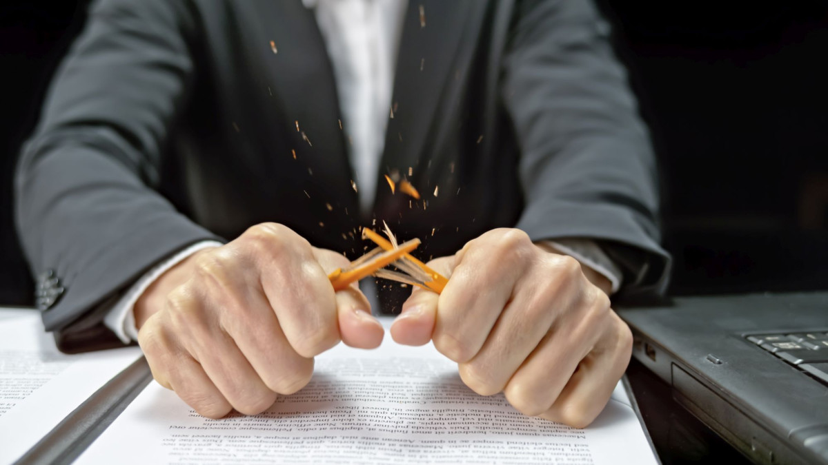 Mann im Anzug zerbricht Bleistift über Verträgen