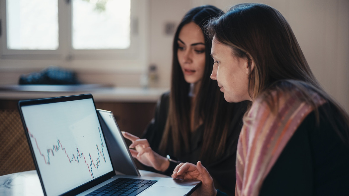 Zwei Frauen blicken auf Laptop mit Börsenkursen.