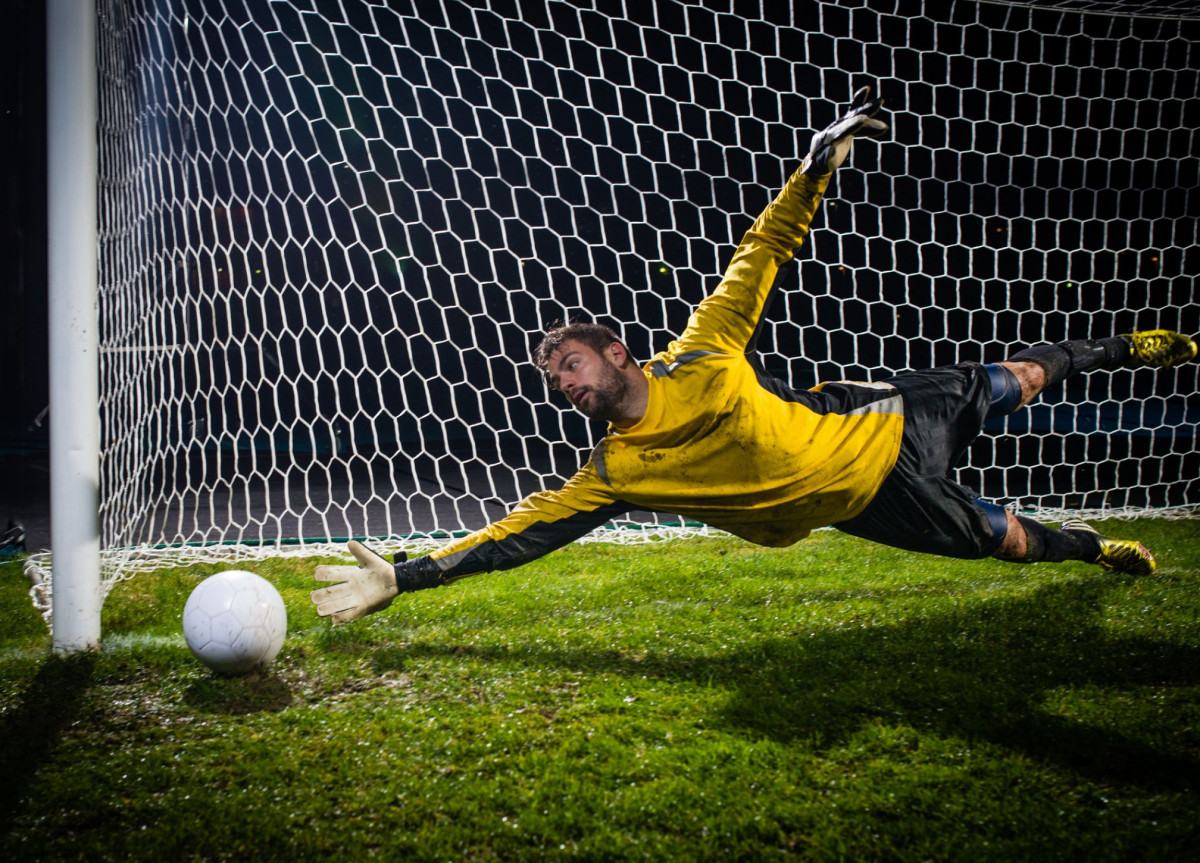 Ein Fußballtorwart hechtet einem Ball hinterher