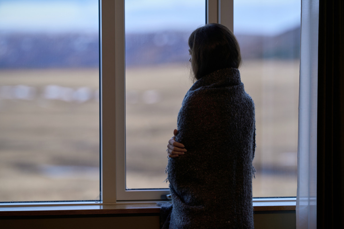 Frau in Decke gehüllt schaut aus dem Fenster