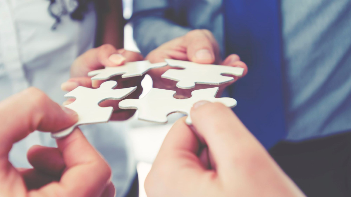 Puzzleteile, die von meherern Händen zusammengesetzt werden