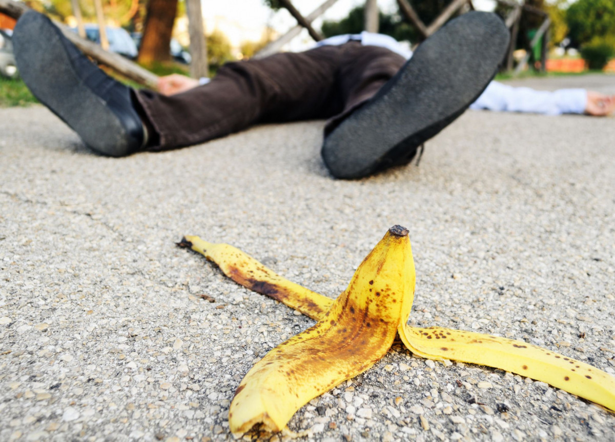 Eine Bananenschale liegt auf einer Straße, dahinter ein Mann, der gerade ausgerutscht ist