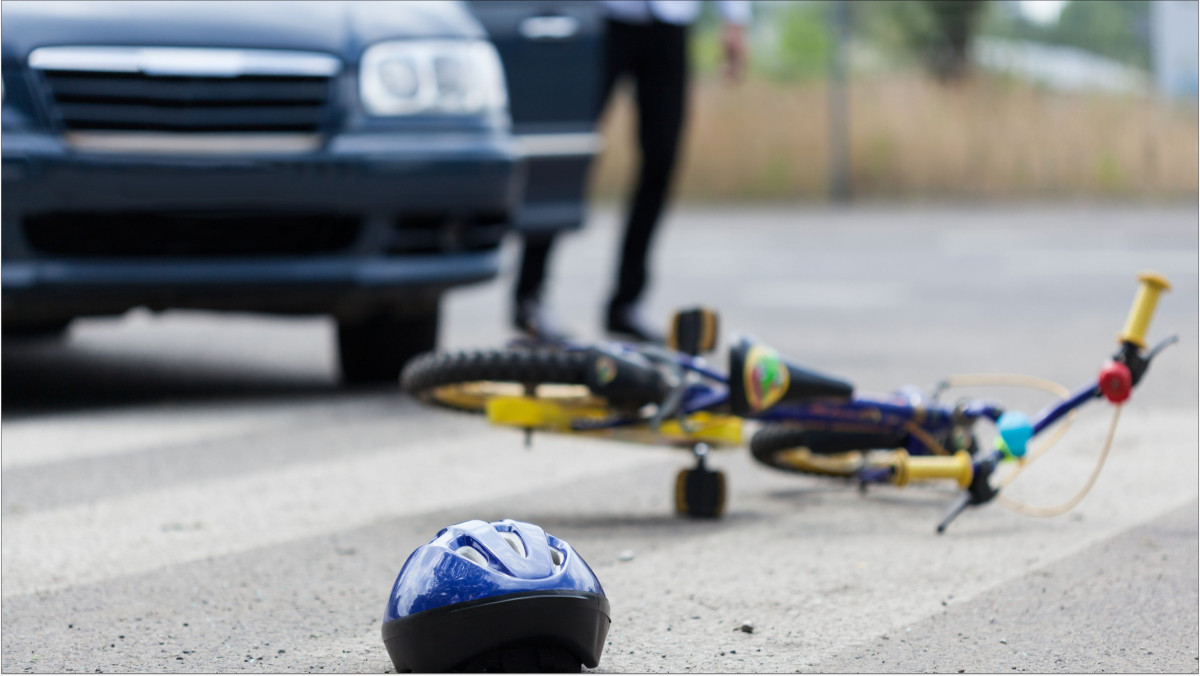 Ein Kinderfahrrad und ein Fahrradhelm liegen vor einem Auto auf der Straße
